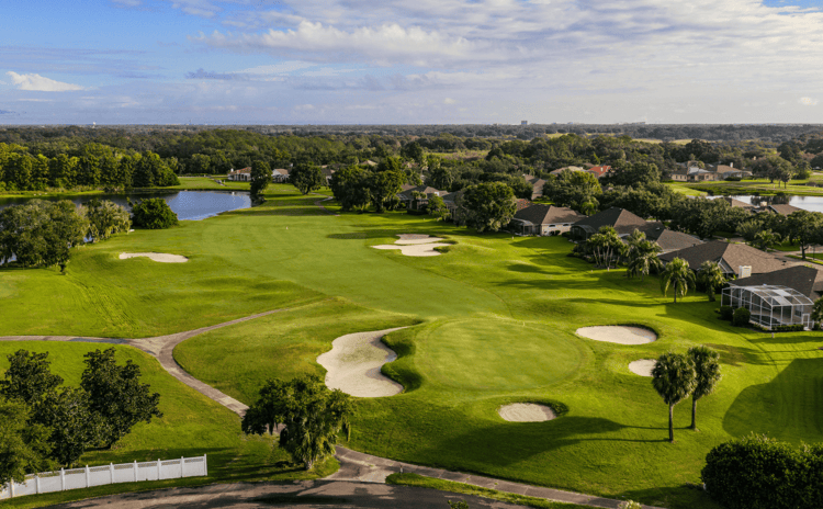 Aerial shot from behind golf course green surrounded by sand bunkers and a long wide fairway in the distance