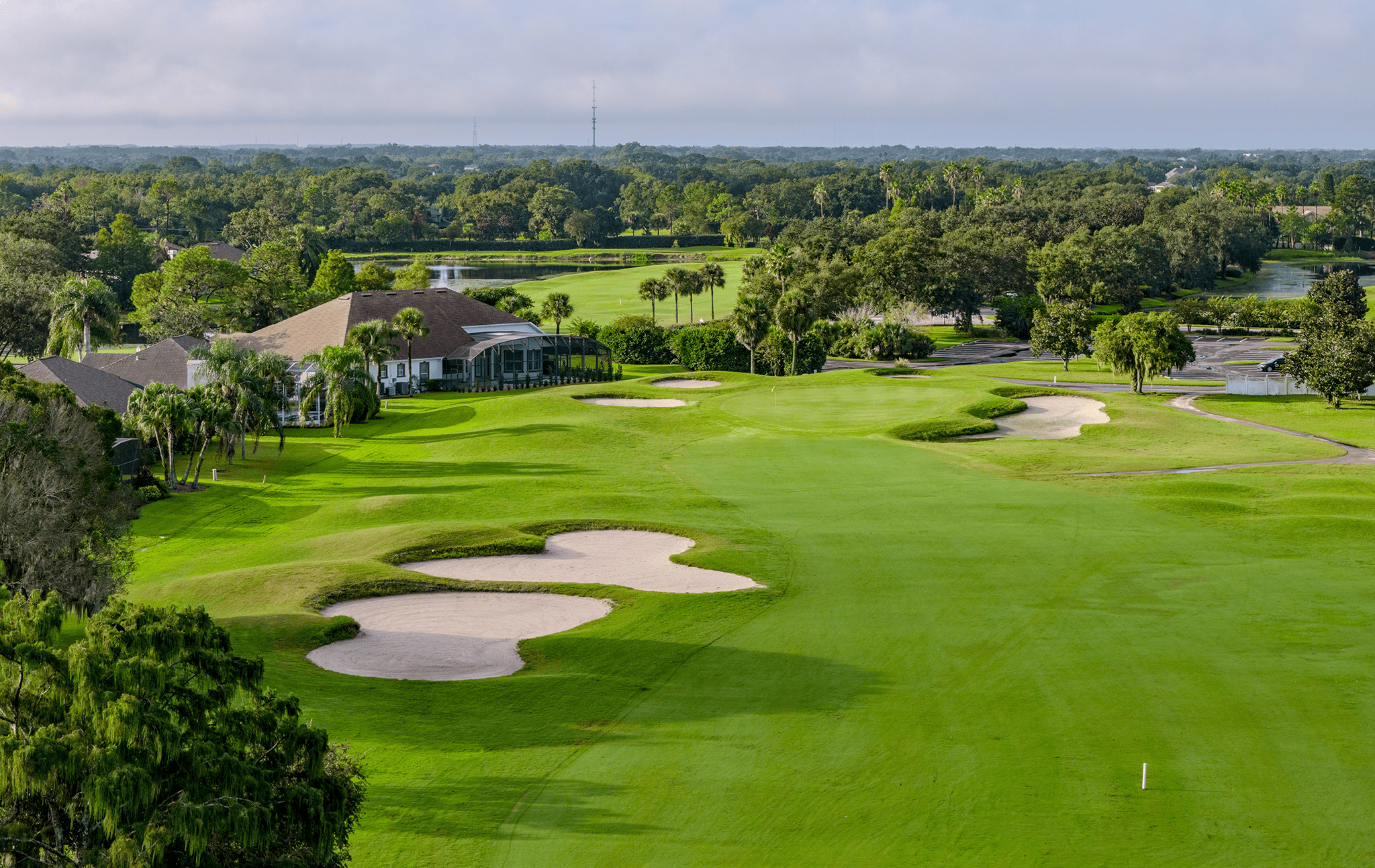 Approach view of green surrounded by sand traps with Kissimmee Bay clubhouse in the distance.